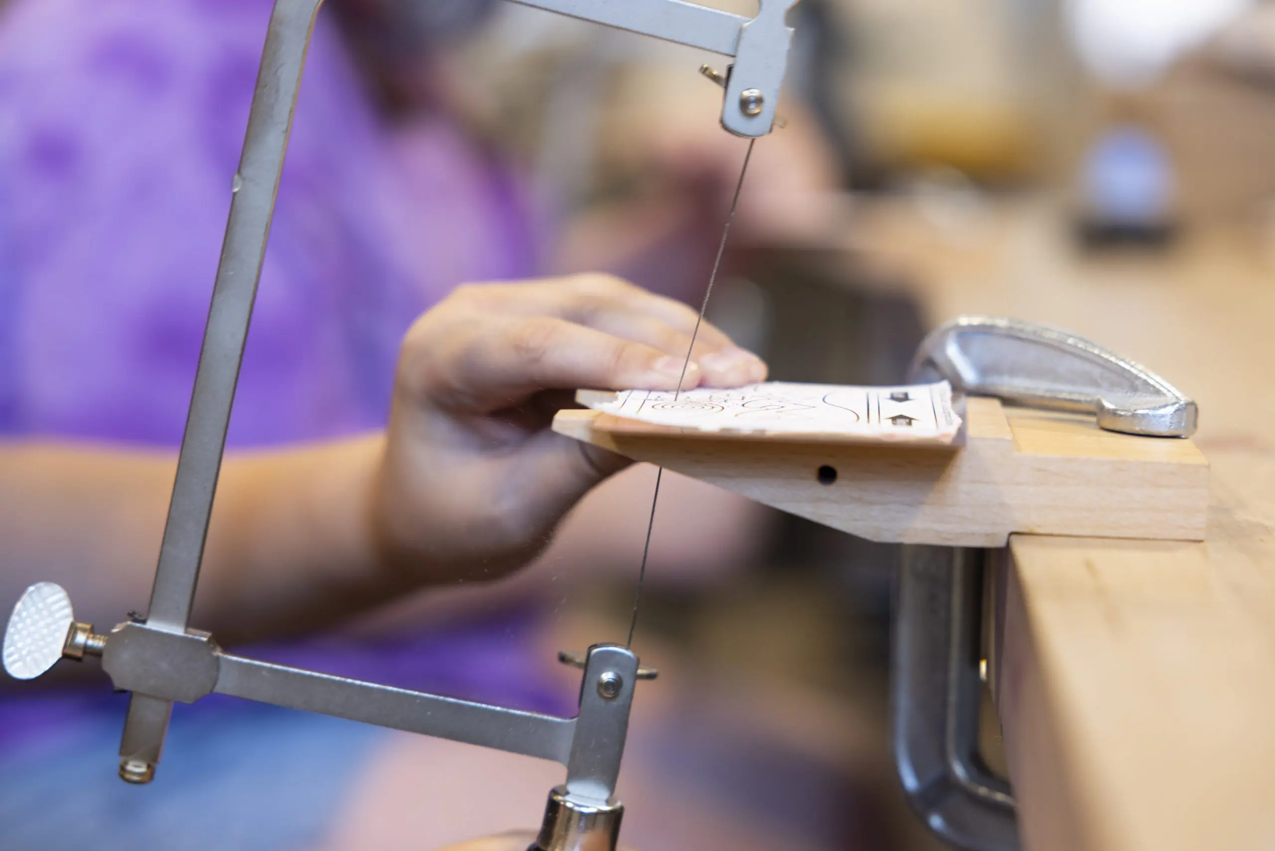 A close-up of a young person's hand bracing a piece of metal on a bench pin while sawing