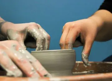 Closeup of two hands forming a clay pot on a pottery wheel