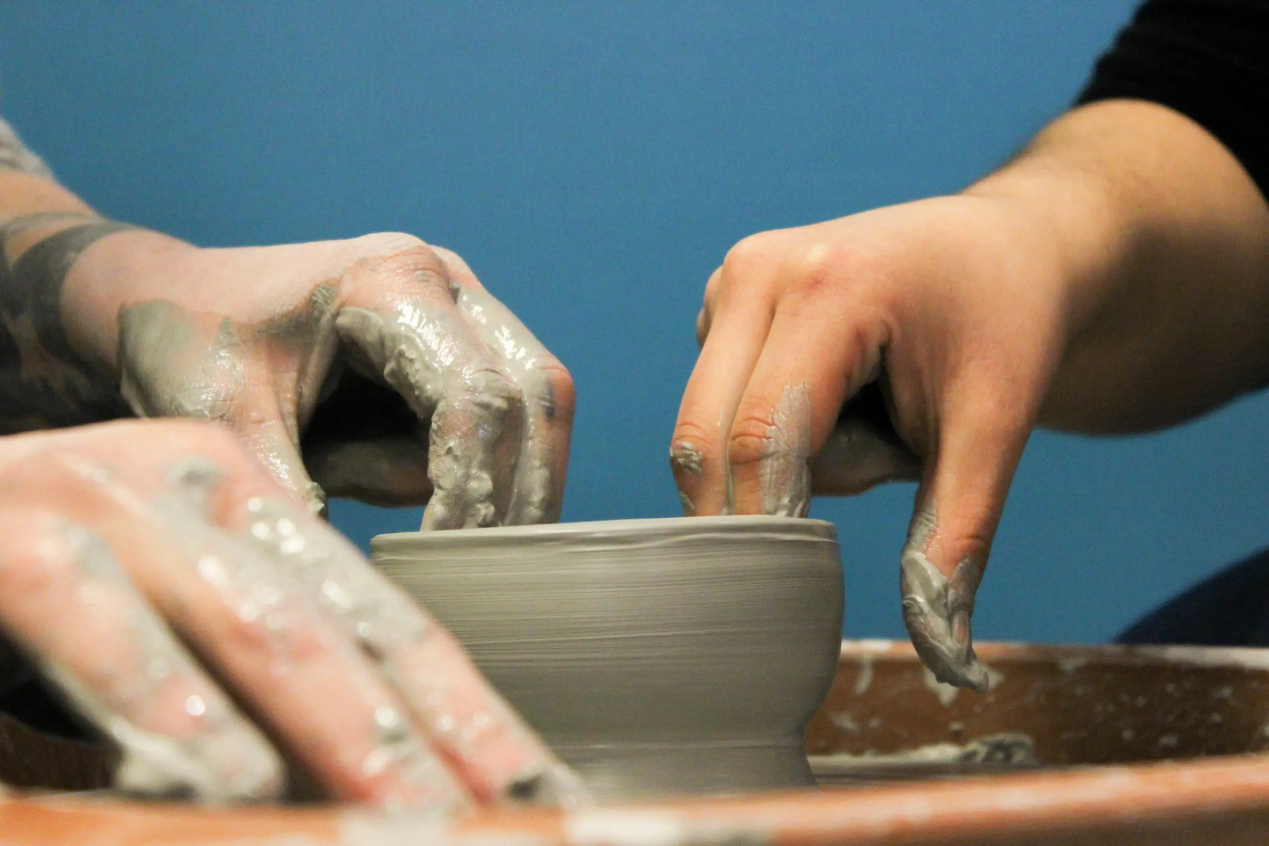 Closeup of two hands forming a clay pot on a pottery wheel