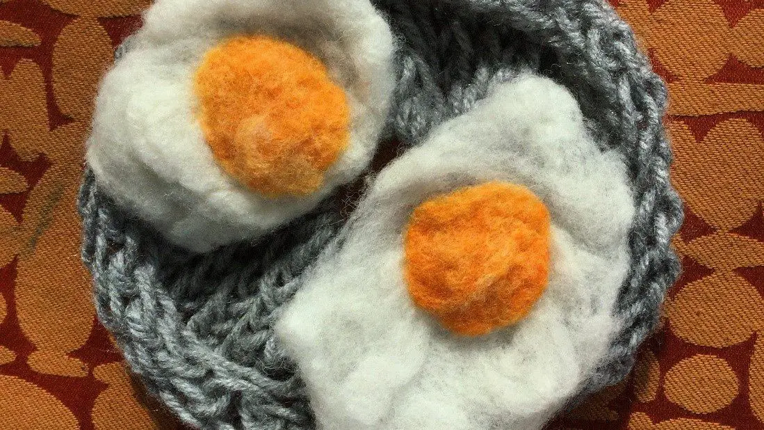 Two felt sunny-side up eggs rest on a knit plate