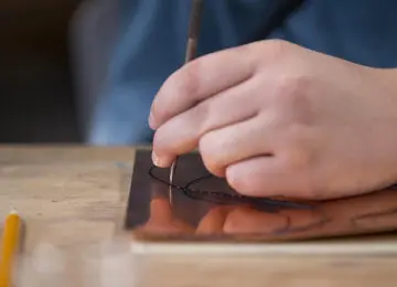 closeup of a hand holding a needle punch on a copper sheet