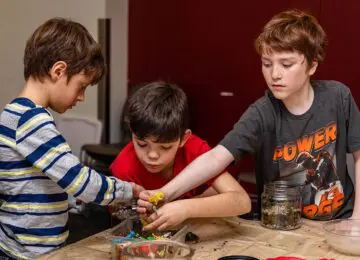 Three tween boys grabbing for plastic building parts at a wooden work table