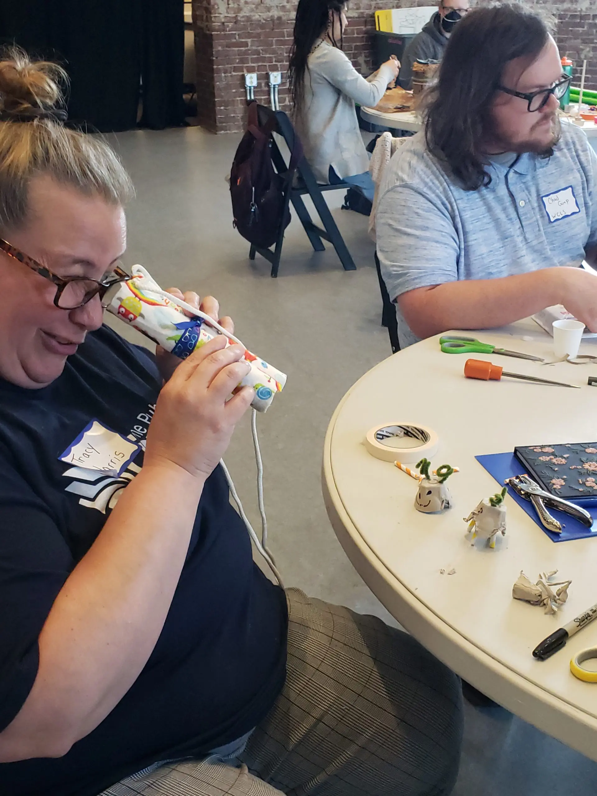 Woman smiling and looking through a cardboard tube at her creations.