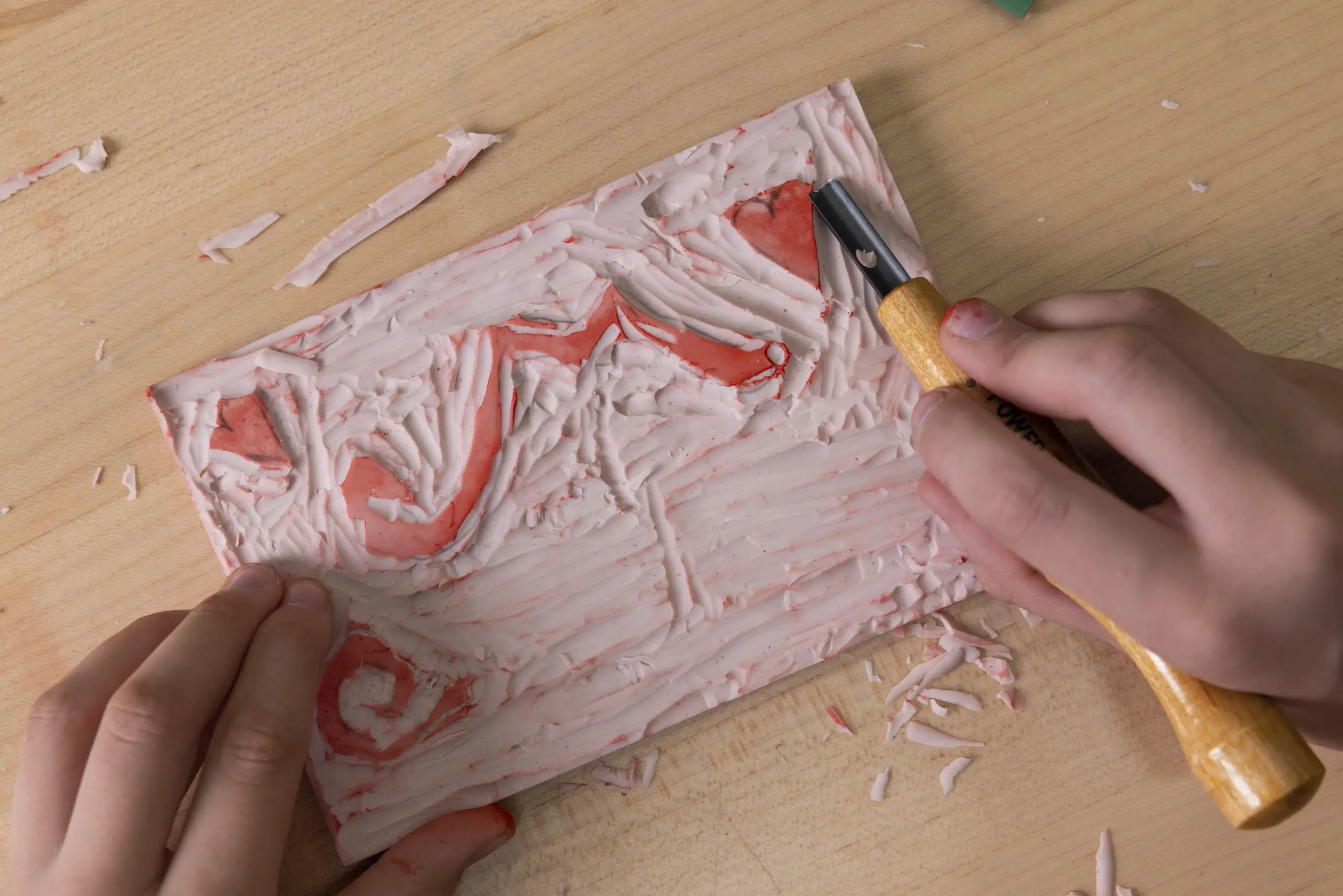 A linocut block is being carved with a u-shaped carving tool