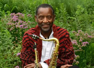 male in red sweater with saxophone in a field