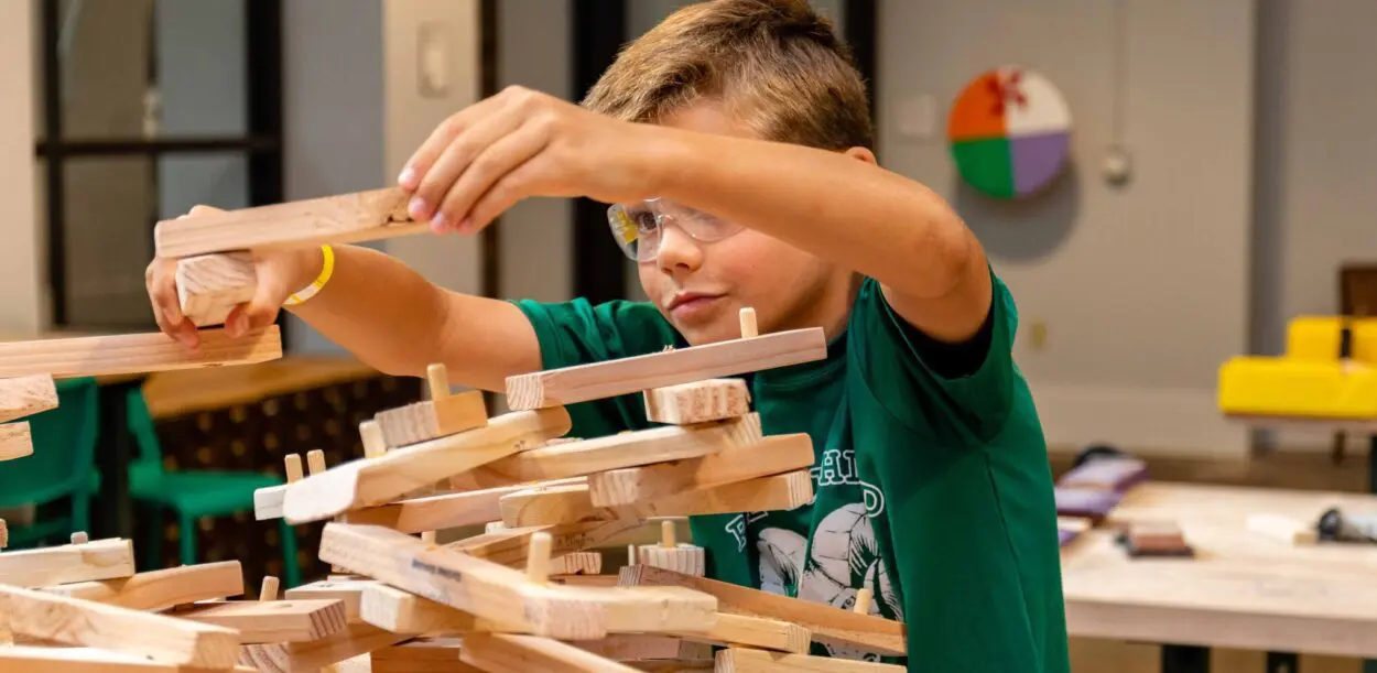 Young boy in safety glasses and a green t-shirt assembling wooden pieces