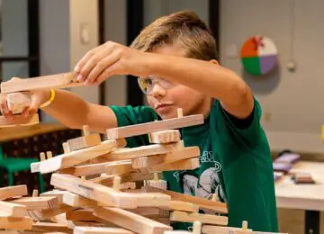 Young boy in safety glasses and a green t-shirt assembling wooden pieces