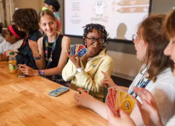 four teen playing cards at a table and laughing