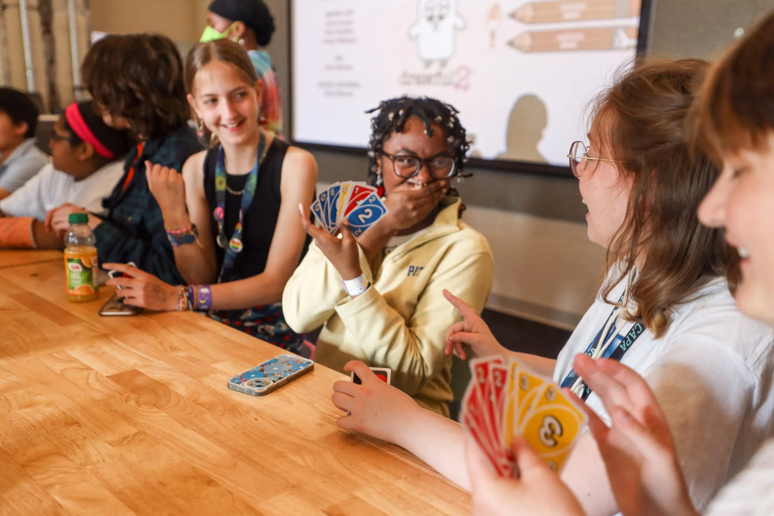 four teen playing cards at a table and laughing