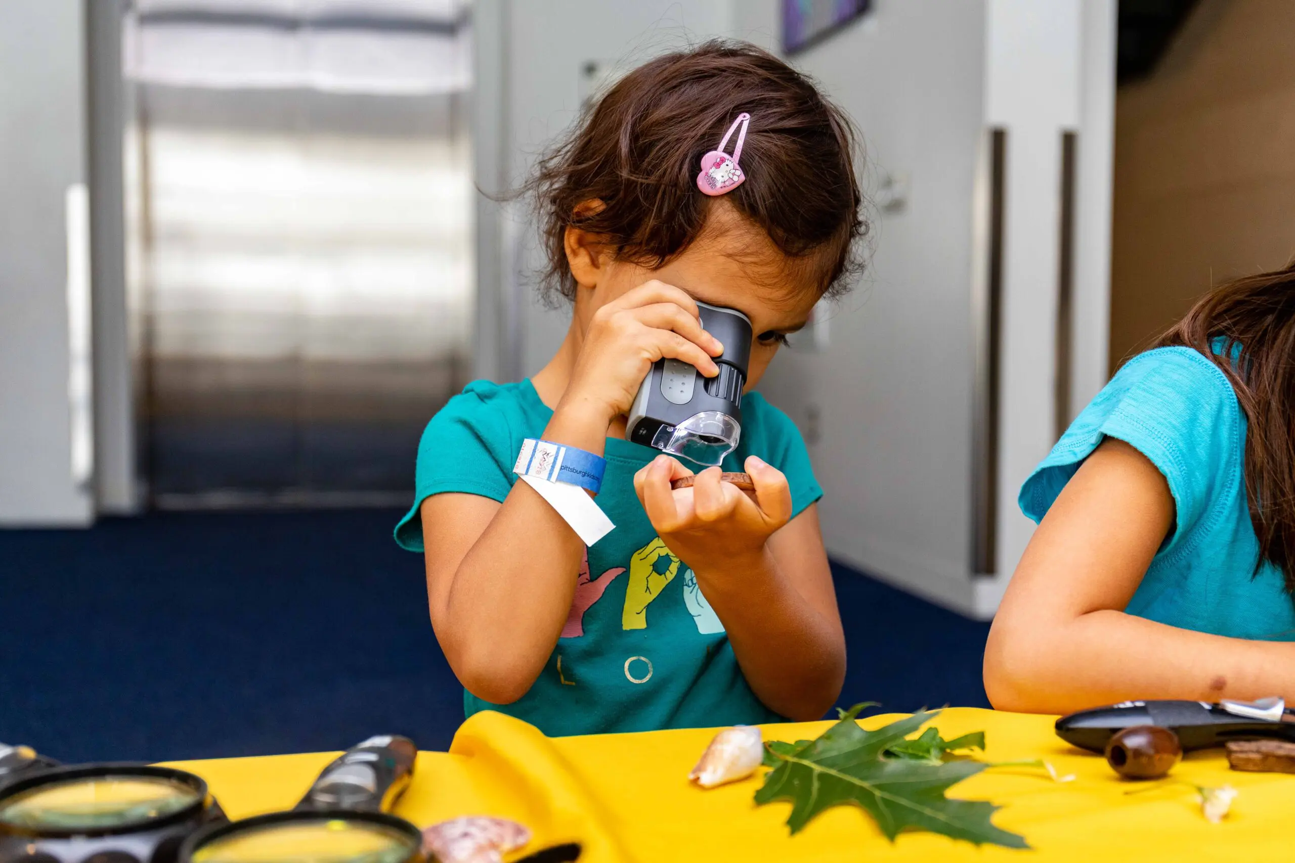 young gilr looking at leaves, shells, rocks, flowers through a small magnifying tool