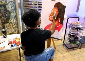 woman sitting and painting a portrait of a woman at an easel