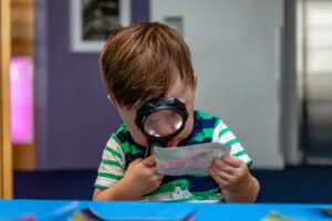 child using a magnifying glass to look at a picture of a frog