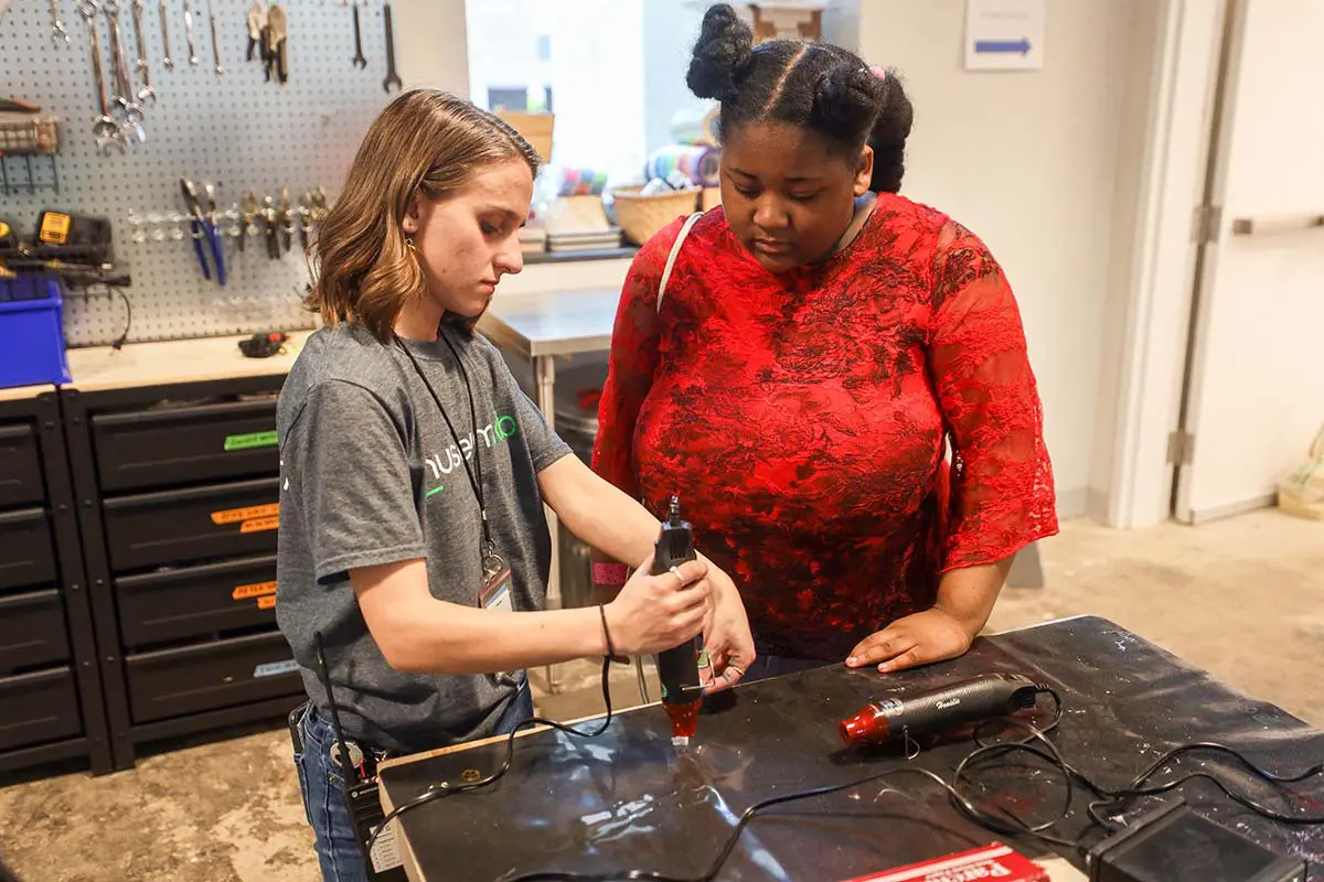 female museum staff helping young girl with heat gun activity