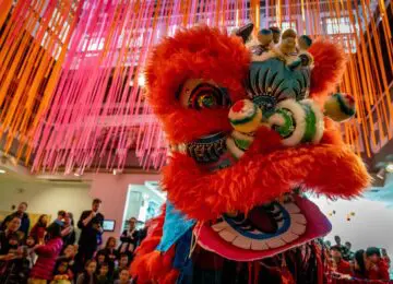 A colorful Chinese lion puppet dances in front of a large crowd in the Art Studio.