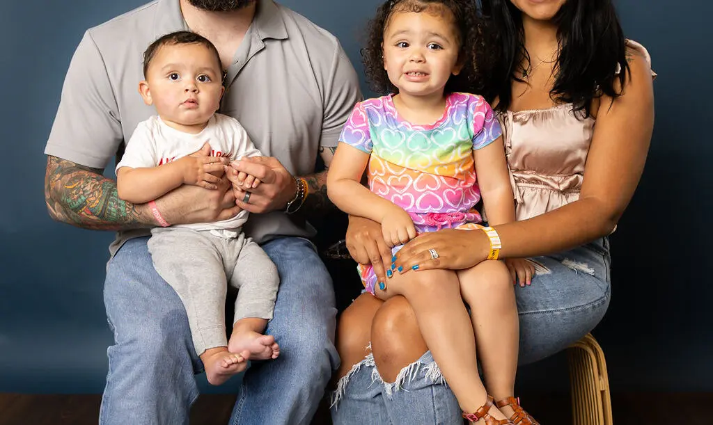 family of two adults, infants and toddler posing against a portrait backdrop