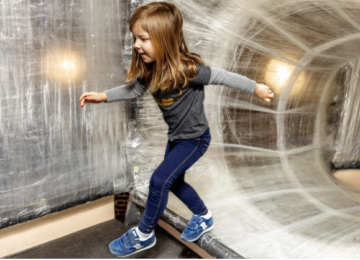 girl in jeans and blue t-shirt running through clear tape tunnel