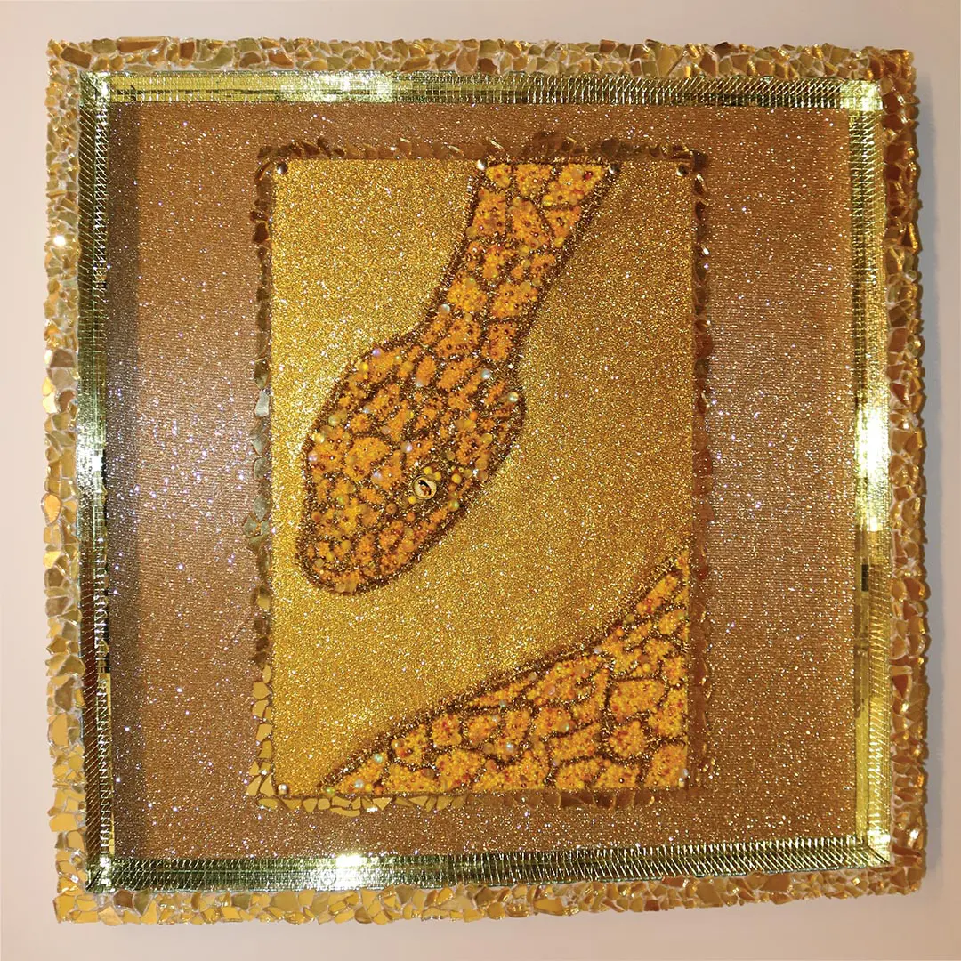 square artwork of gold beaded art featuring a snake's head