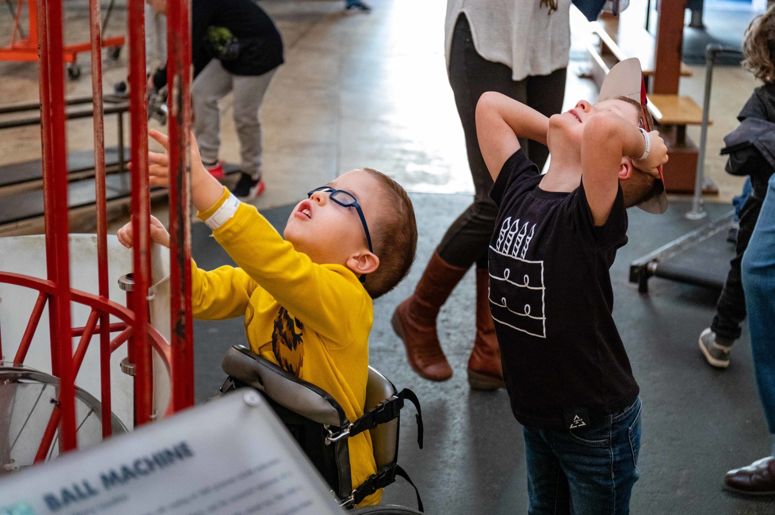 Two young boys looking up at a ball balancing interactive in the garage. One boy is in a wheelchair, one is standing behind him