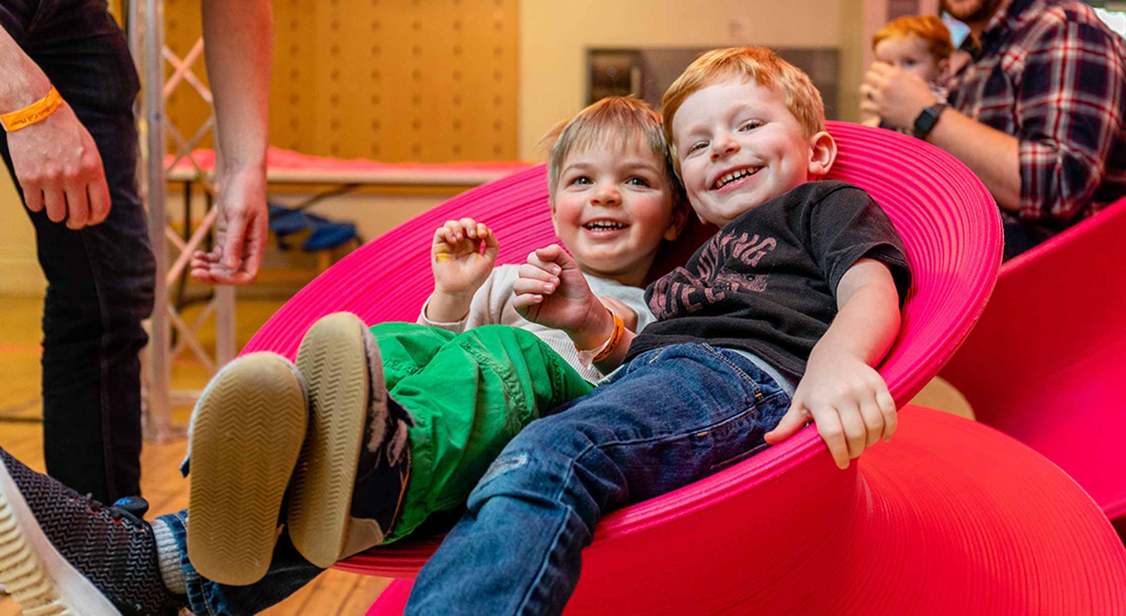 two boys reclining in red spinny chair and smiling