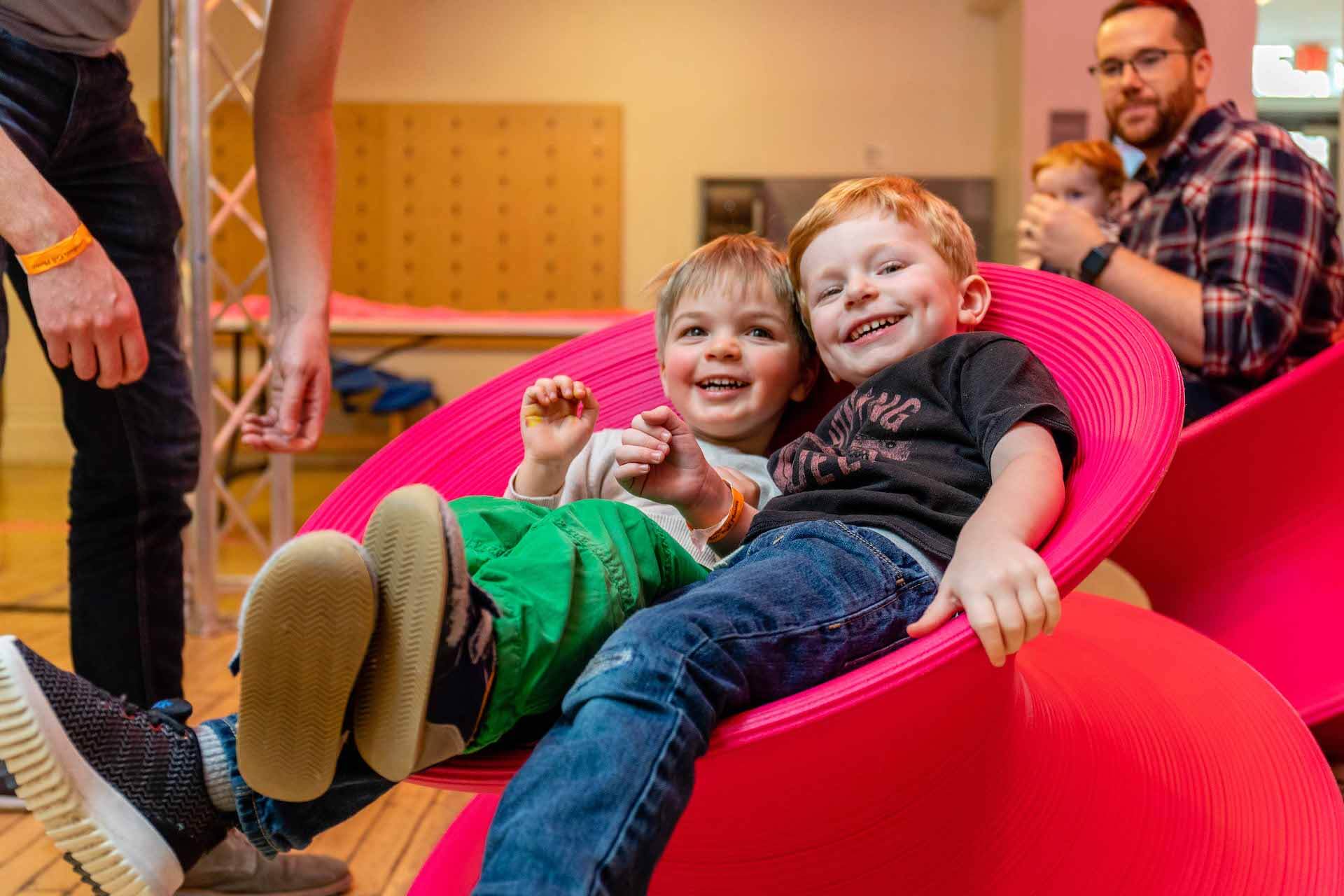 two blond boys reclining in a red spinny chair