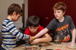 Three tween boys grabbing for plastic building parts at a wooden work table