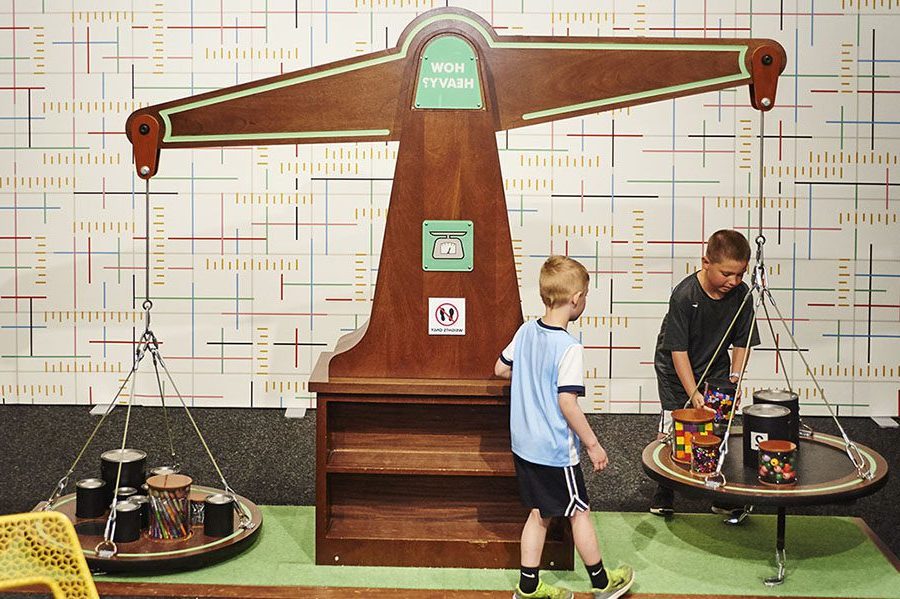two boys transfer large paint cans between the sides of a giant balancing scale