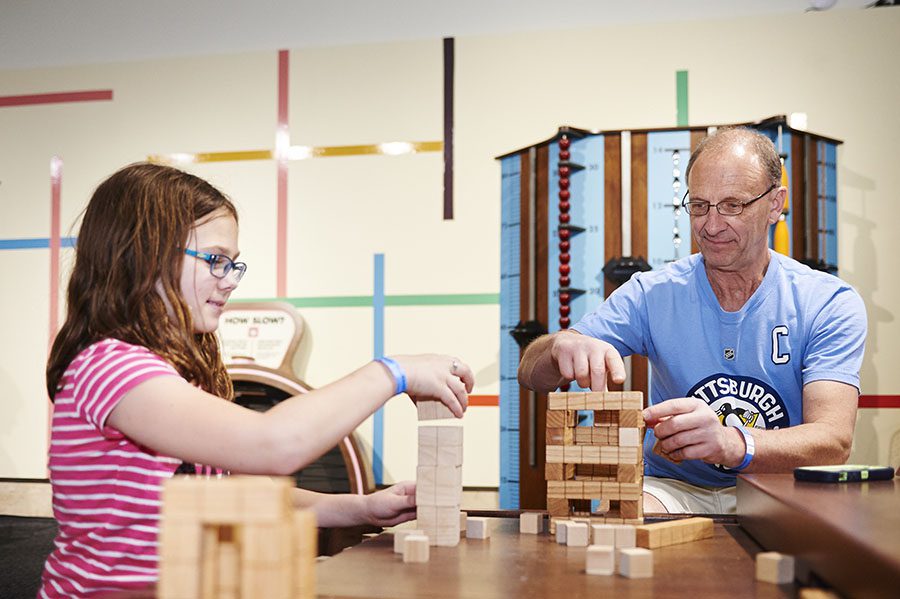 adult and girl measuring with wooden blocks at a table