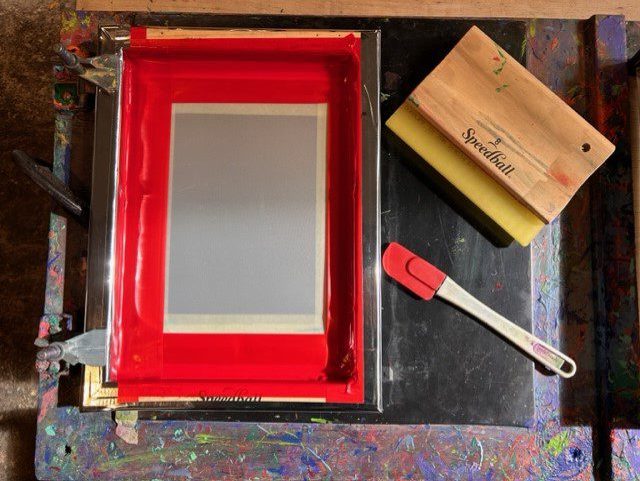 An aerial view of a screen used for screen printing, an ink squeegee, and a rubber spatula is shown.