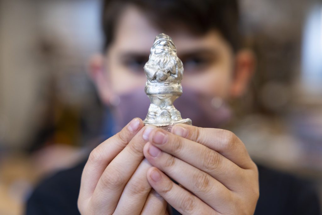 A child holds a small pewter cast of a garden gnome.
