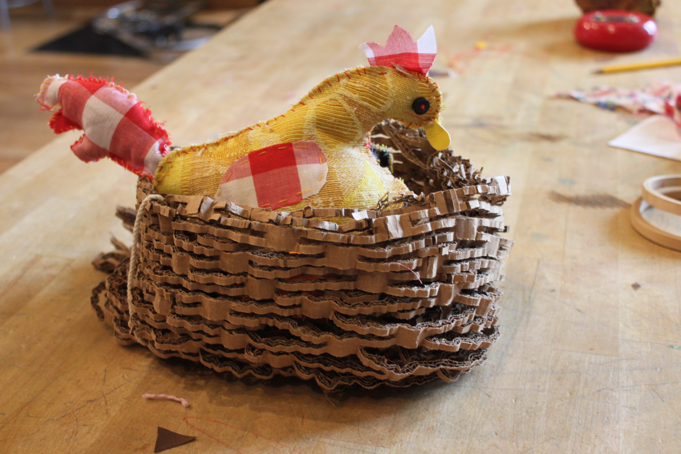 A hand sewn stuffed chicken sits in a recycled paper nest.