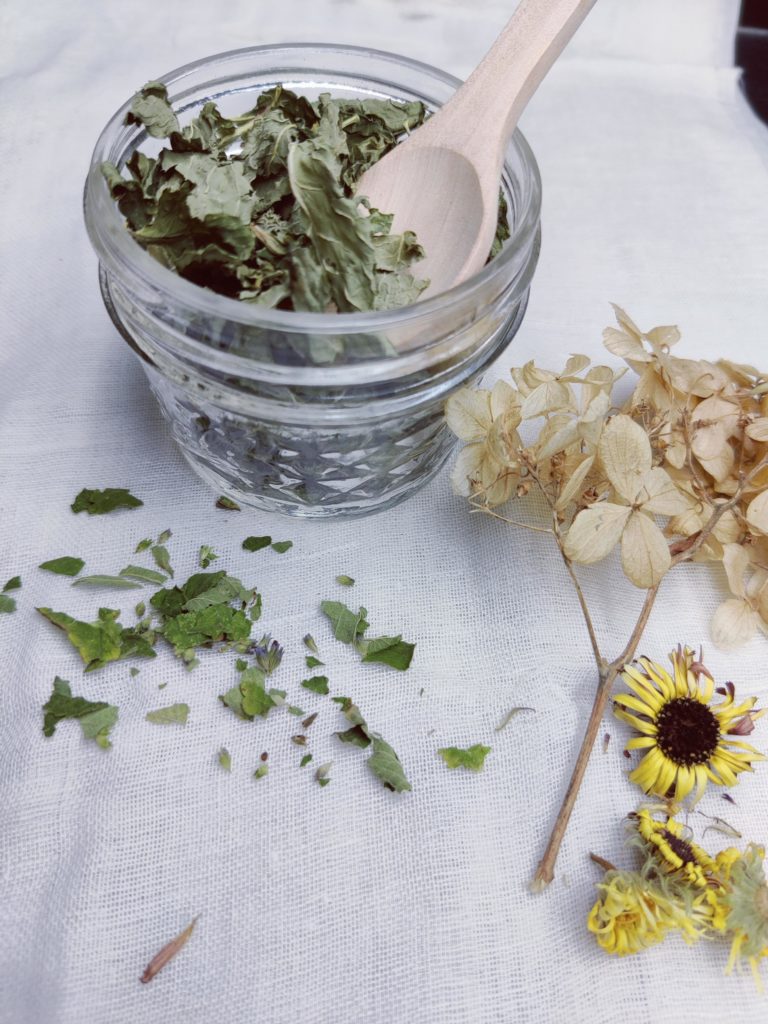 A glass jar filled with dried leaves and two types of dried flowers sit on a white table.