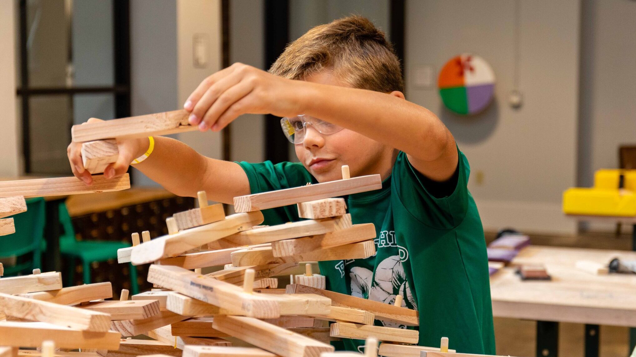 Young boy in safety glasses and a green t-shirt assembling wooden pieces