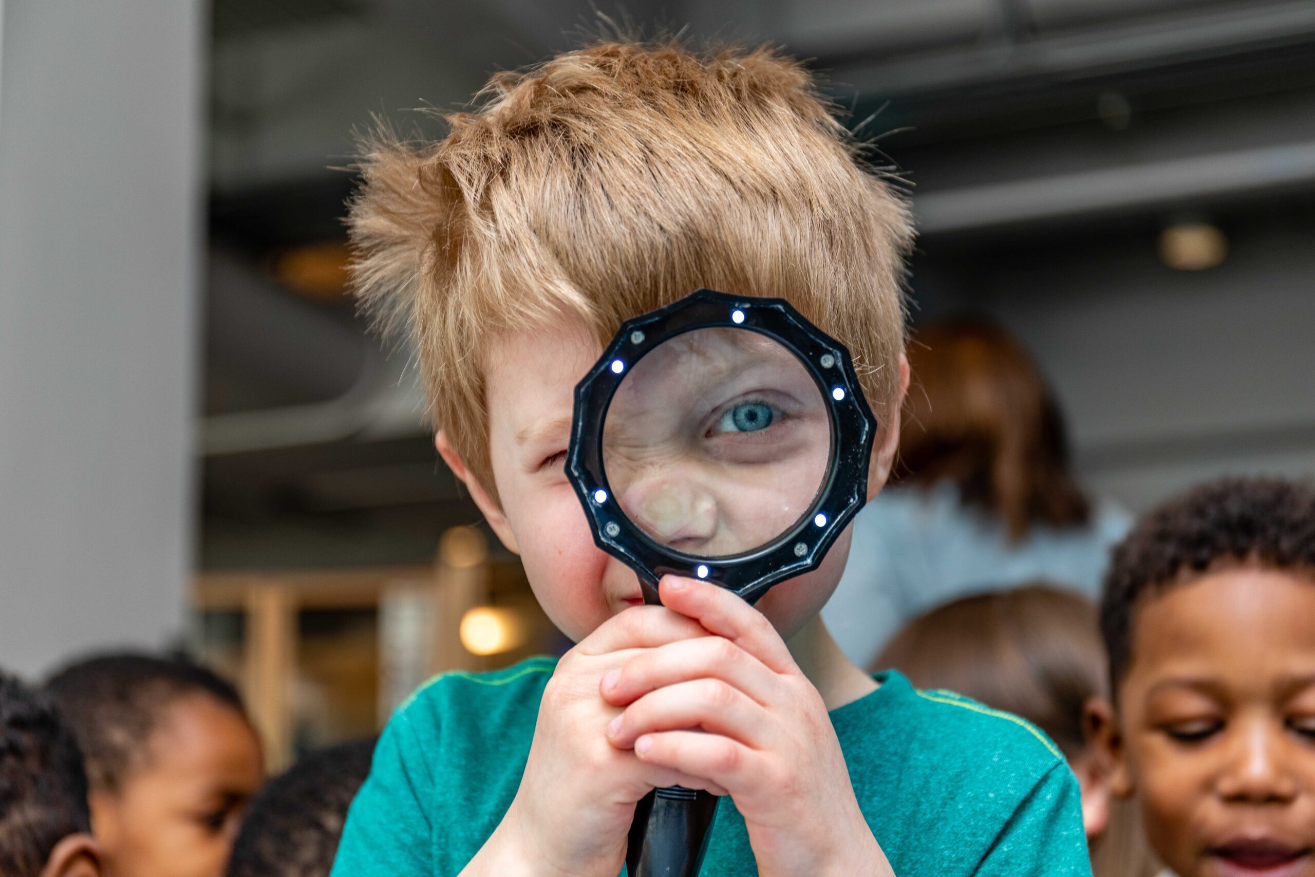 A child looks through a magnifying glass into the camera