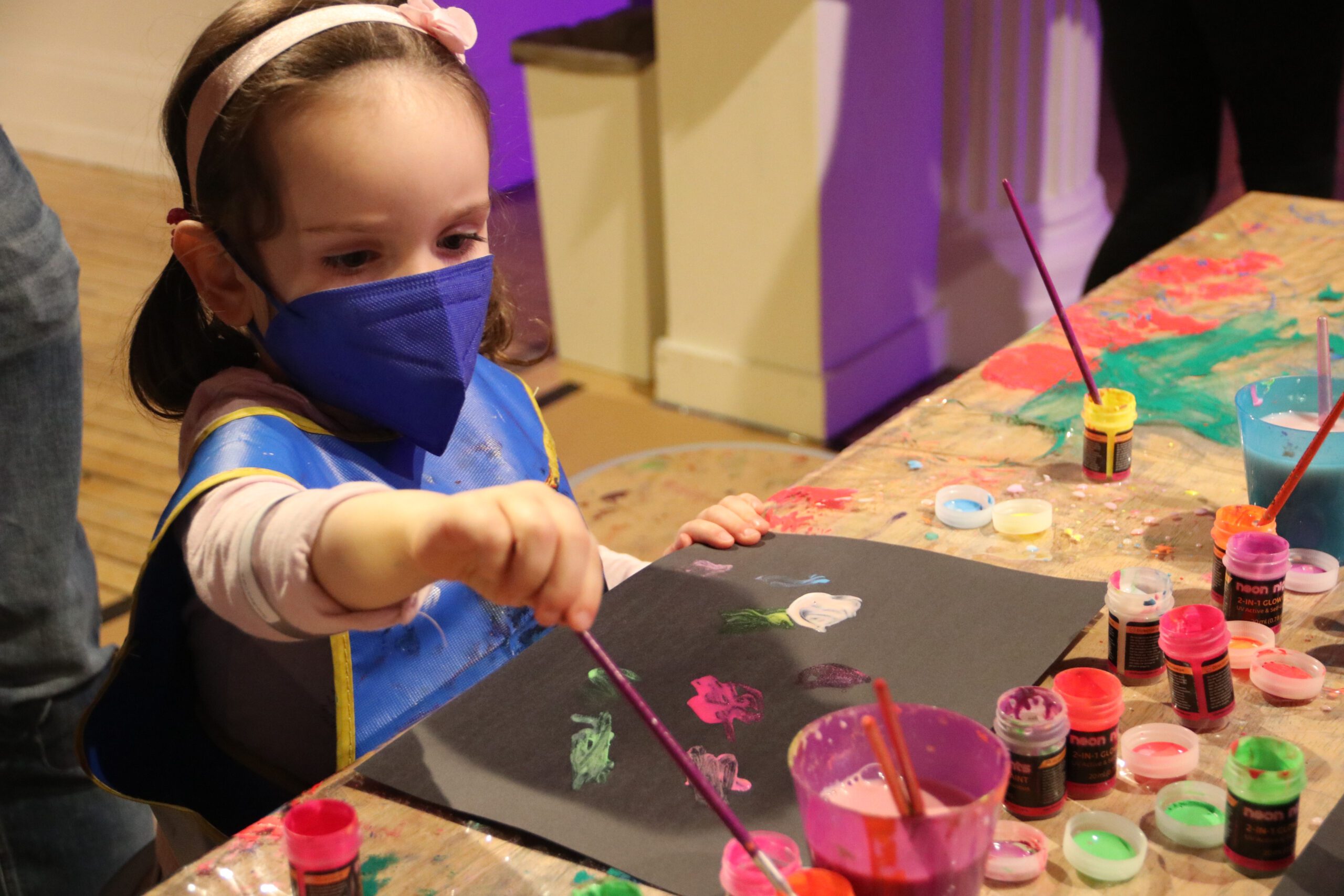 A child uses neon colored paints to paint on a black canvas