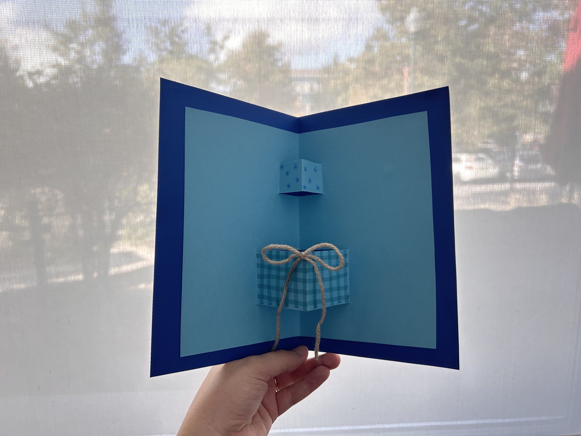 A hand is holding a blue card with two pop-out presents