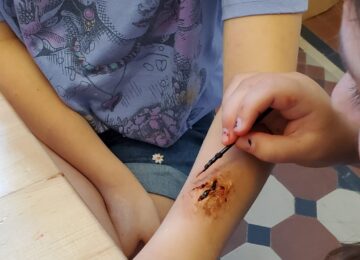 A workshop participant applies makeup on another participant's arm to create a fake wound