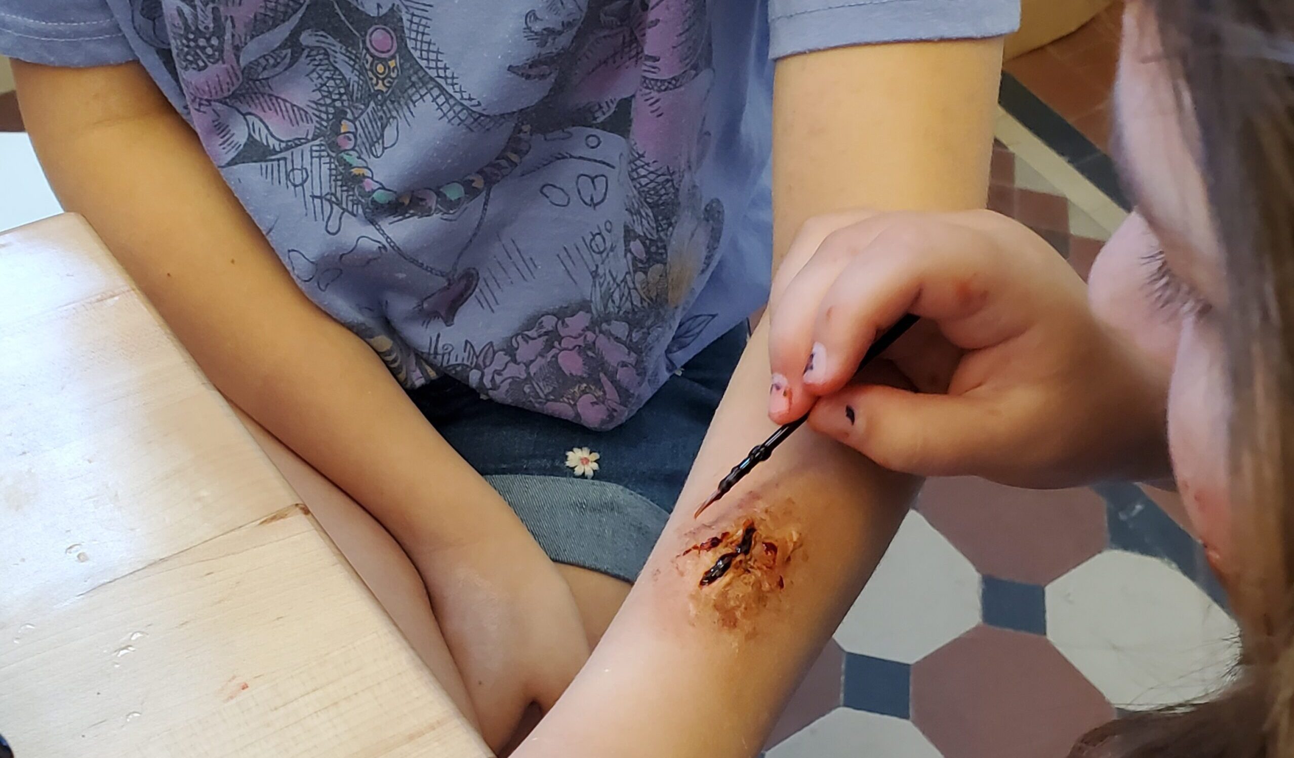 A workshop participant applies makeup on another participant's arm to create a fake wound