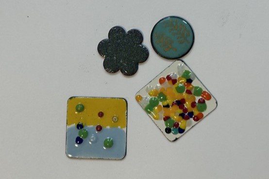 four small enameled pieces sit on a white surface