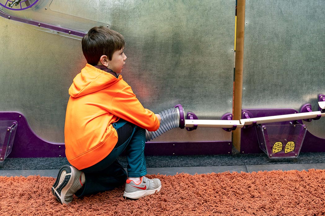 boy crouching at channel mounted against a wall to create a Rube Goldberg machine
