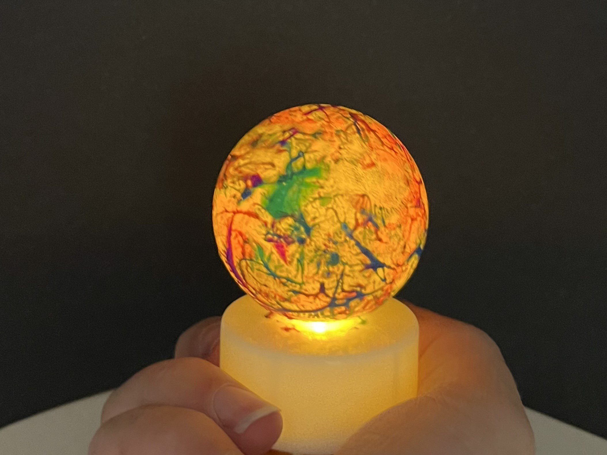 a ball splatter-painted with neon colors in lit from inside with a tealight