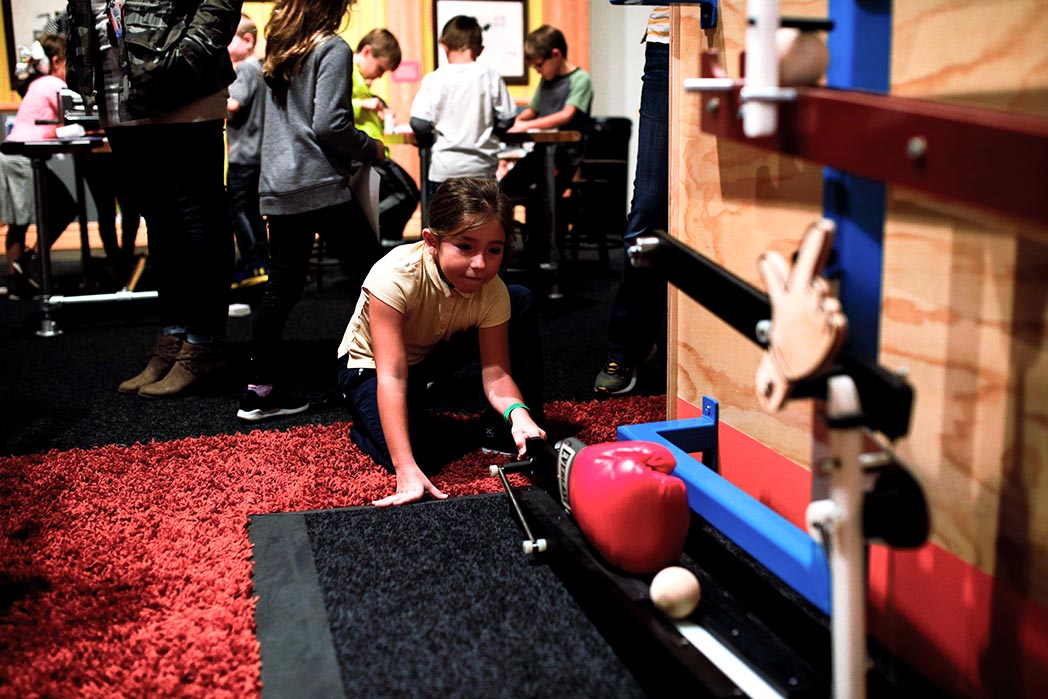 Girl crouching to set a ball in motion on a Rube Goldberg machine