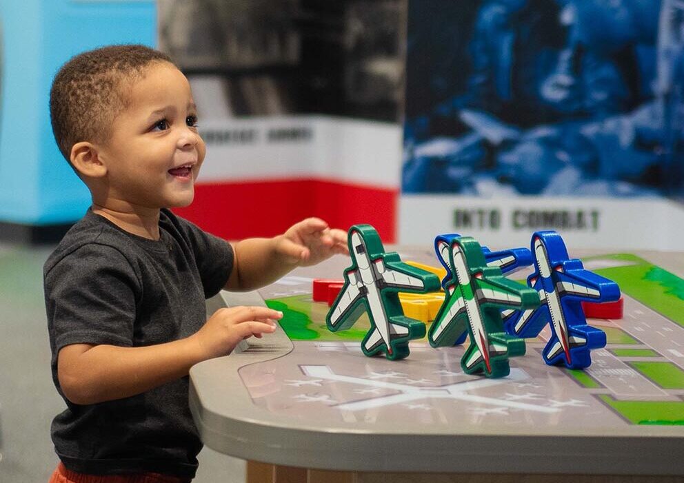 Boy at table with wooden plane figures in Aim High exhibit
