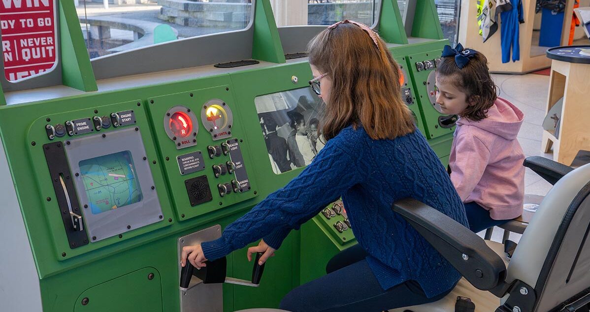 two young girls at a green airplane console with switches