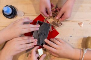 Three sets of hands work together to stamp shapes out of metal.