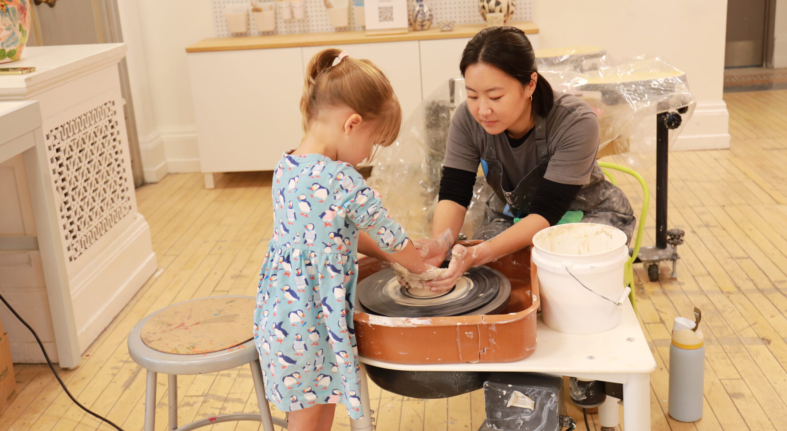 educator helps young girl mold clay on a wheel